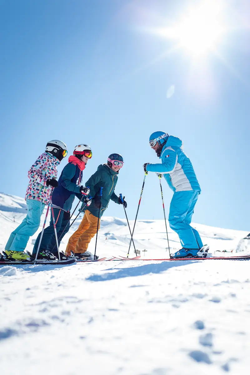 moniteur de ski expliquant le planté du bâton à trois élèves — tous parfaitement alignés, l’air concentré, comme s’ils s’apprêtaient à participer à une cérémonie secrète. le moniteur démontre le geste avec un sérieux imperturbable, tandis que les élèves tentent d’imiter le mouvement sans transformer la scène en numéro d’orchestre désynchronisé