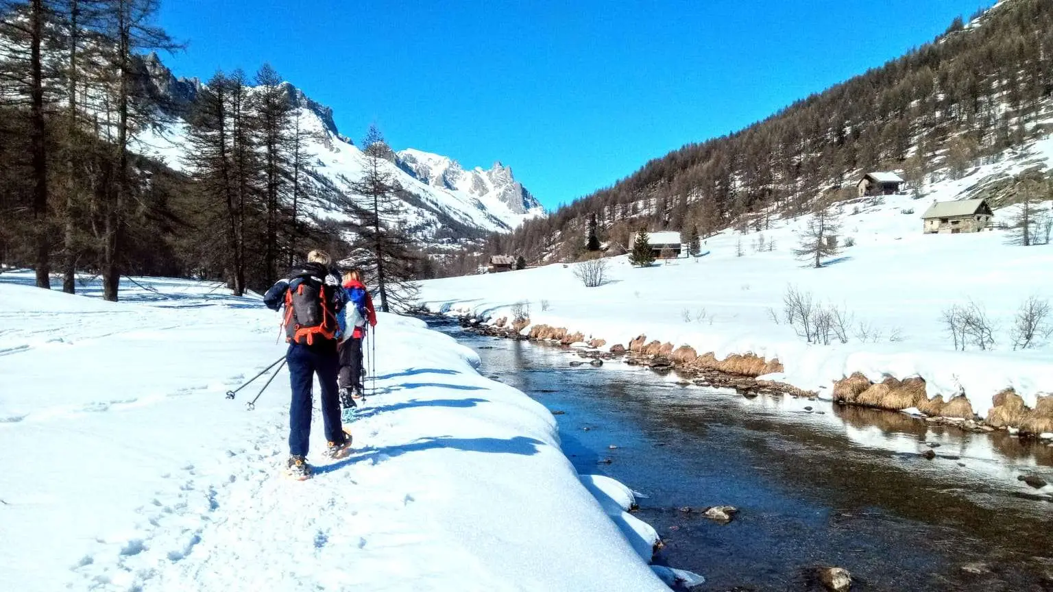 Randonneurs en raquettes traversant la haute vallée de la Clarée sous un grand soleil, entourés de montagnes enneigées.
